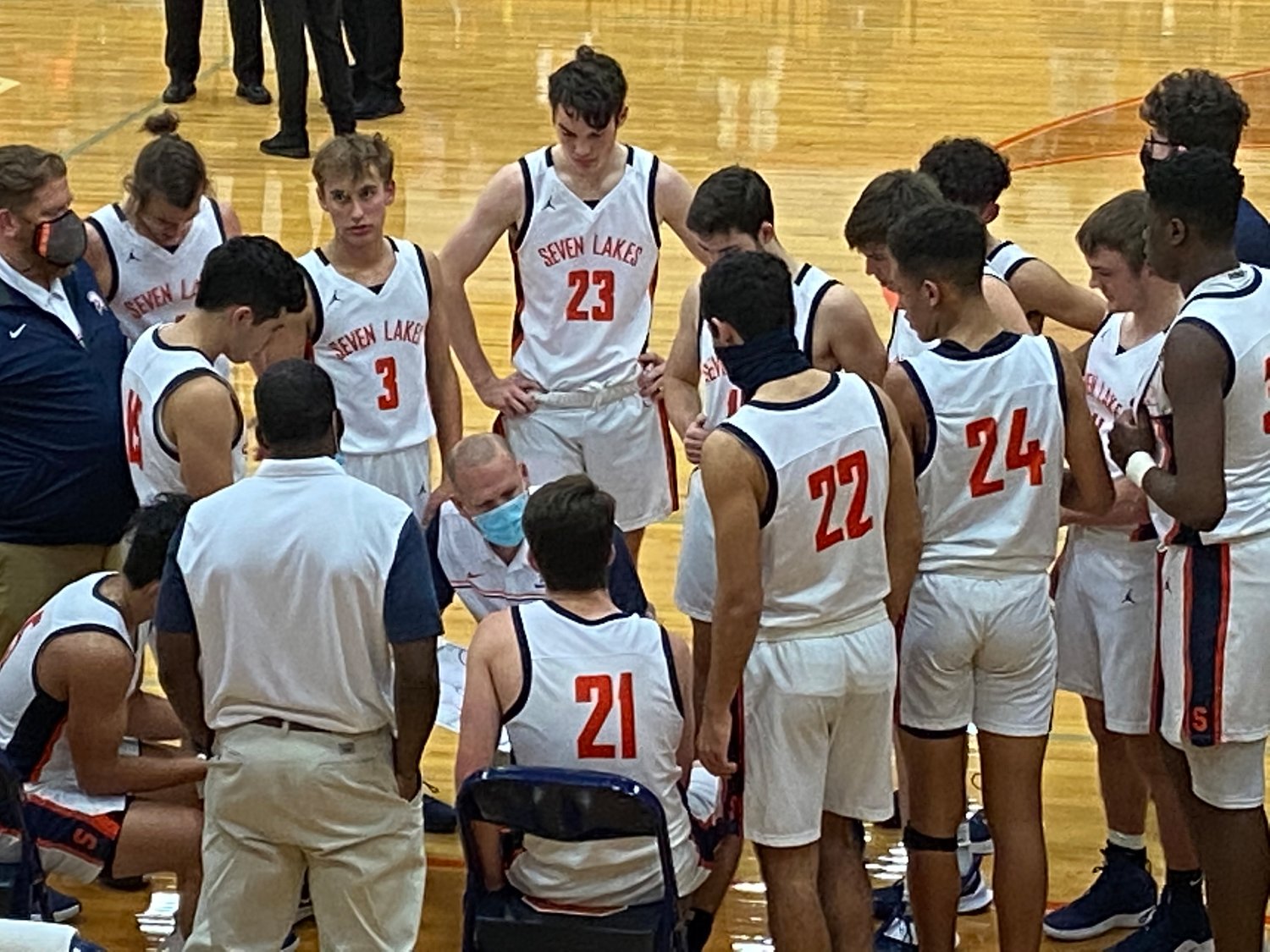 Seven Lakes boys basketball coach Shannon Heston, kneeling in the mask, talks to his players during a timeout during a game against Taylor on Jan. 12 at Seven Lakes High.