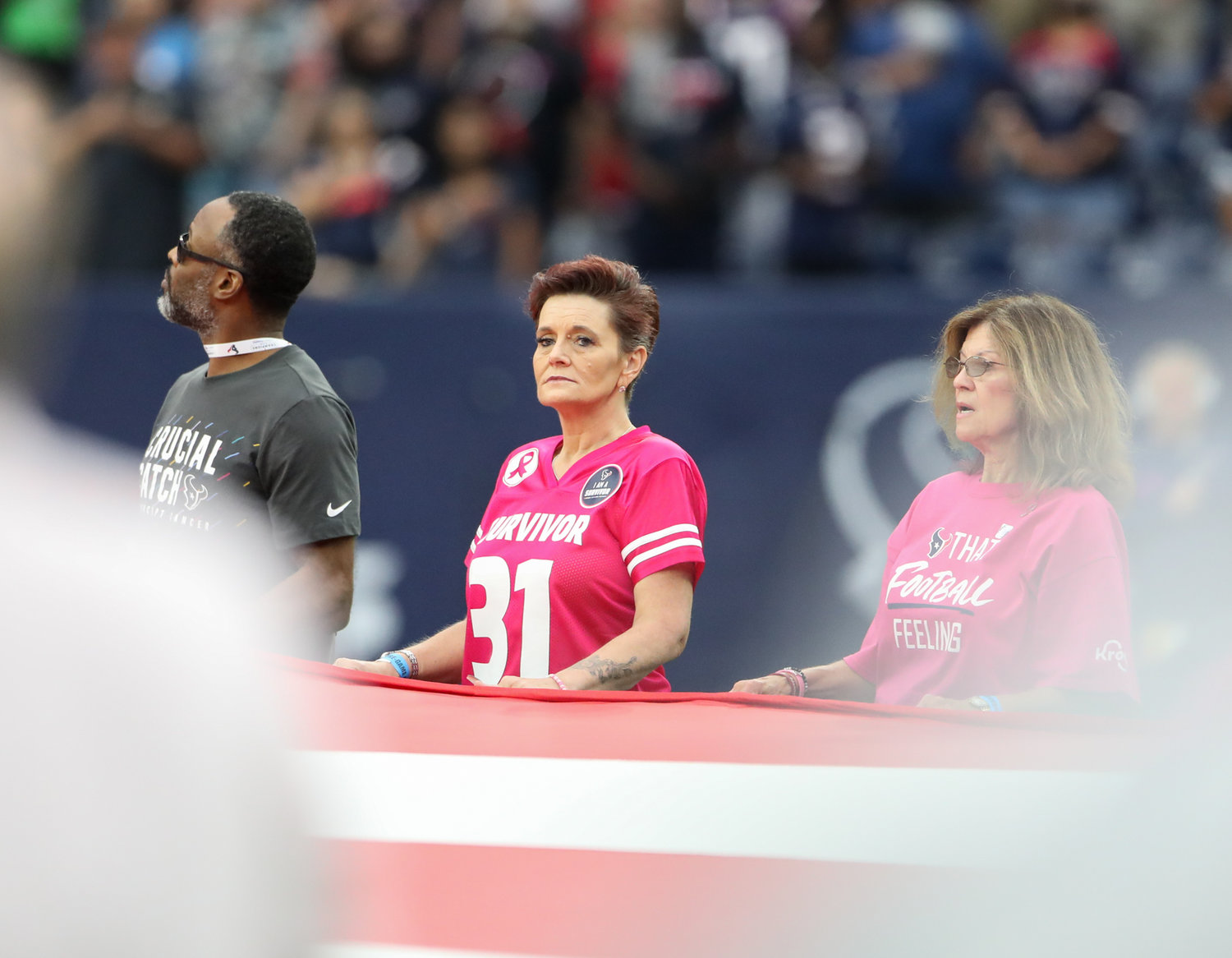 Cancer survivors hold the flag during the national anthem before the start of an NFL game between Houston and New England on “Pink Ribbon Day” October 10, 2021 in Houston, Texas. The Patriots won 25-22.