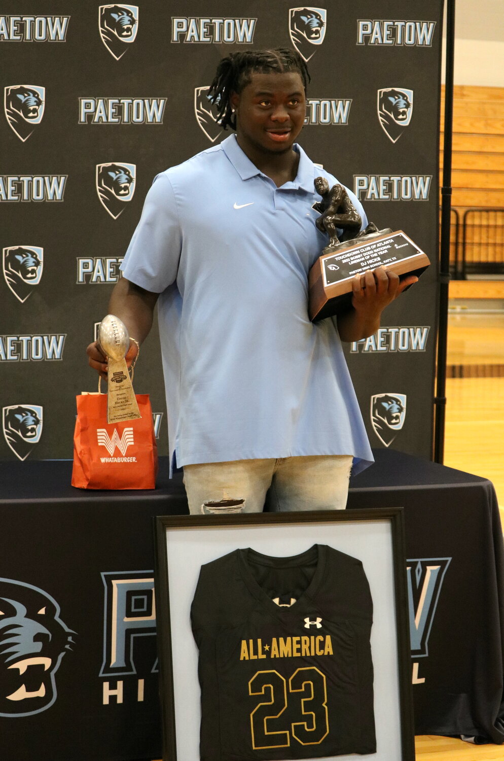 D.J. Hicks holds up his National Lineman of the Year and Whataburger Team of the Year Trophy while also being presented with a frame of his All-American jersey.