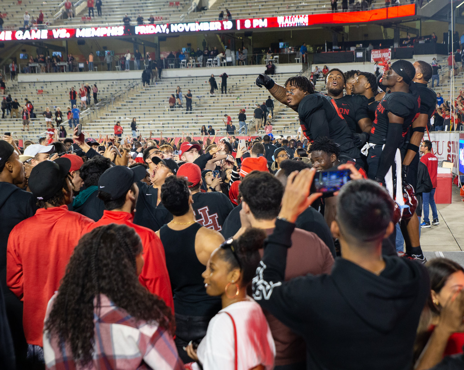 A group of Houston Cougars players celebrate on the field with fans after a 44-37 win over rival SMU in an NCAA football game on October 30, 2021 in Houston, Texas.